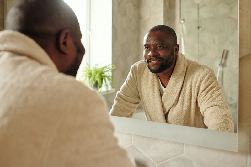 A man in a robe looking at his reflection in the mirror